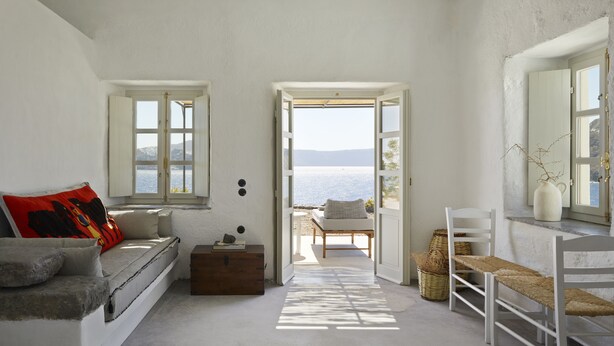A room with a view of the sea, a wooden bench, a white sofa, and a small table with a vase.