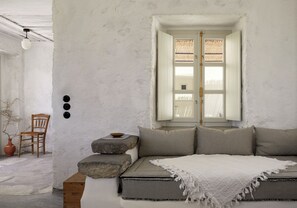 Una habitación con una cama, una silla, un ventanal y una lámpara de pared.