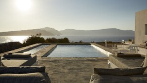 A pool area with lounge chairs and a view of the sea and mountains.