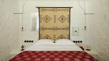 A bed with a patterned headboard, a red bedspread, and a wall-mounted picture frame.