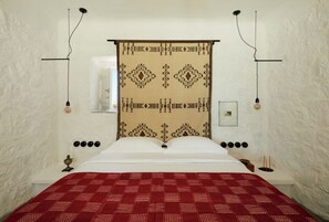 A bed with a patterned headboard, a red bedspread, and a wall-mounted picture frame. - Santa Irini Retreat (Therasia)
