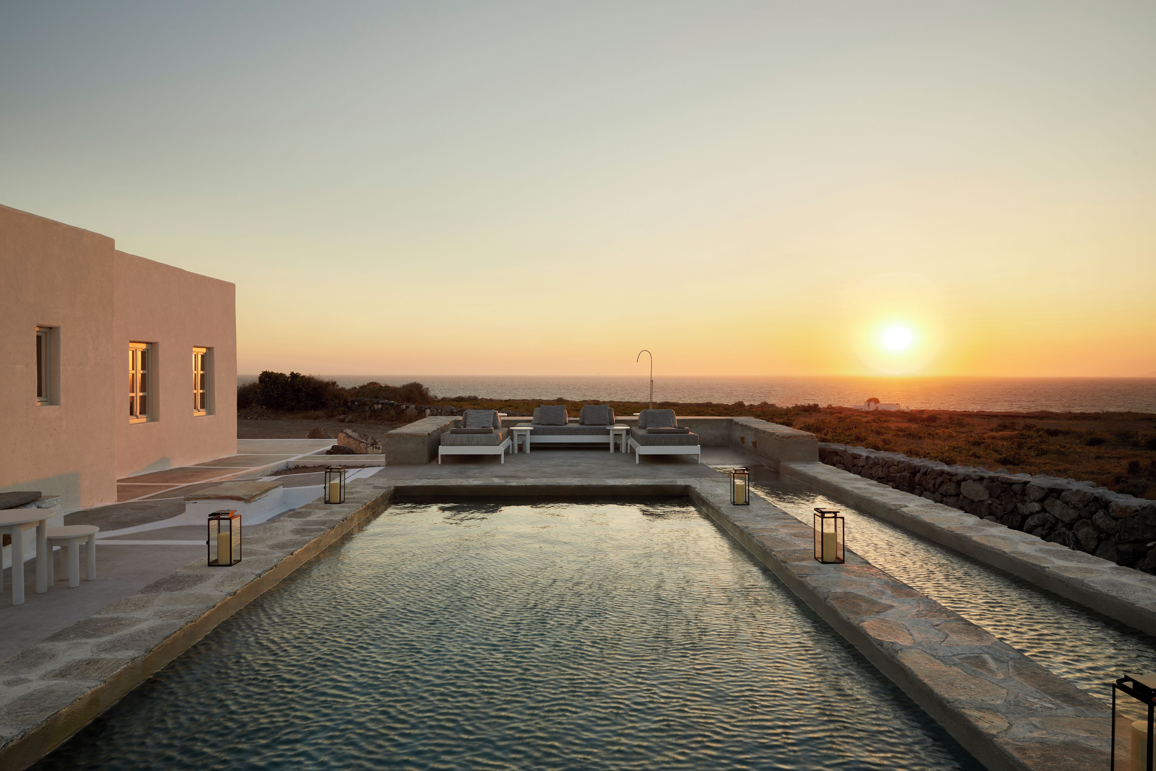 A modern outdoor pool area with lounge chairs and a view of the sunset over the sea.