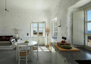 A modern kitchen with a dining area, white walls, and a view of the sea. - Santa Irini Retreat (Therasia)