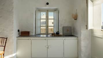 Une cuisine avec des meubles blancs, une chaise en bois et une fenêtre donnant sur un bâtiment blanc.
