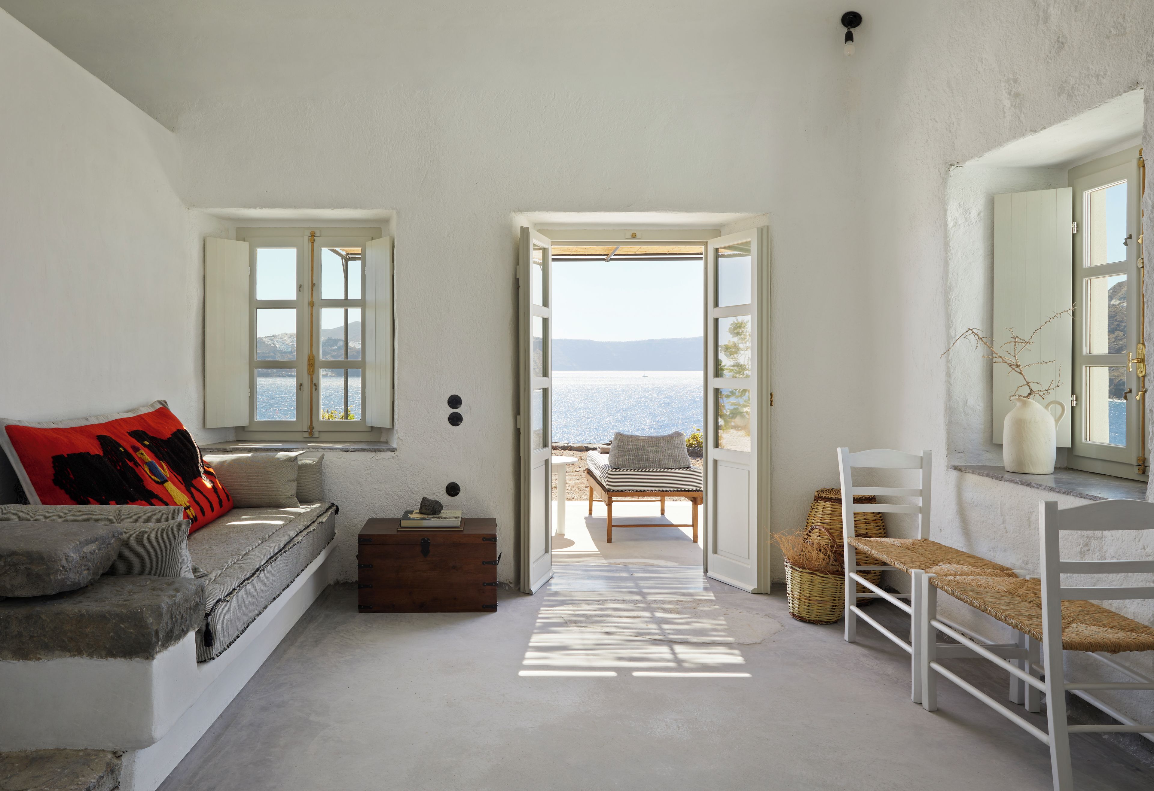 A room with a view of the sea, a sofa, a wooden chest, and a wicker chair.