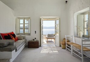 Una habitación con vista al mar, un sofá, un cofre de madera y una silla de mimbre.