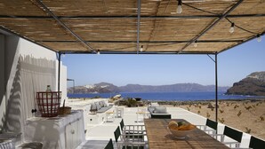 A covered outdoor seating area with a view of the sea and mountains.