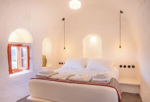 A bedroom with a bed, a bench, and a window with a view. - Santa Irini Retreat (Therasia)