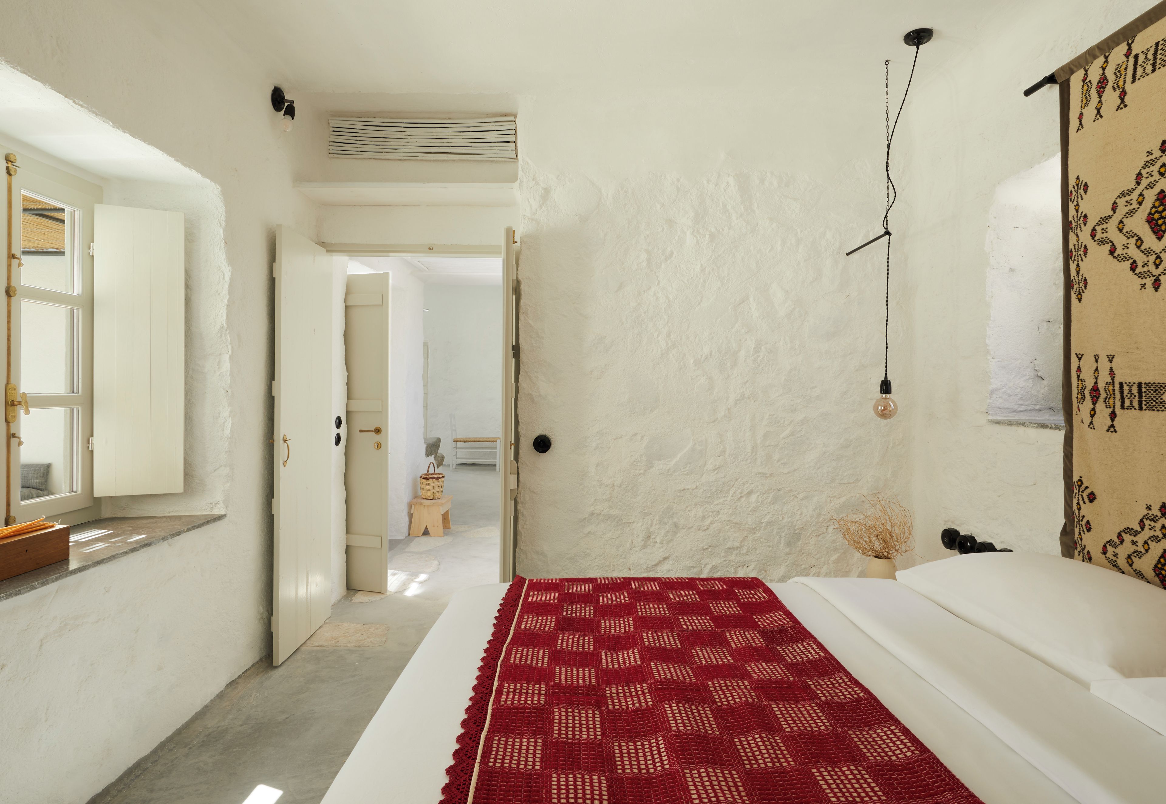 A bedroom with a bed, a red patterned rug, a white wall, and a hanging light fixture.