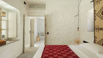 A bedroom with a bed, a red patterned rug, a white wall, and a hanging light fixture.