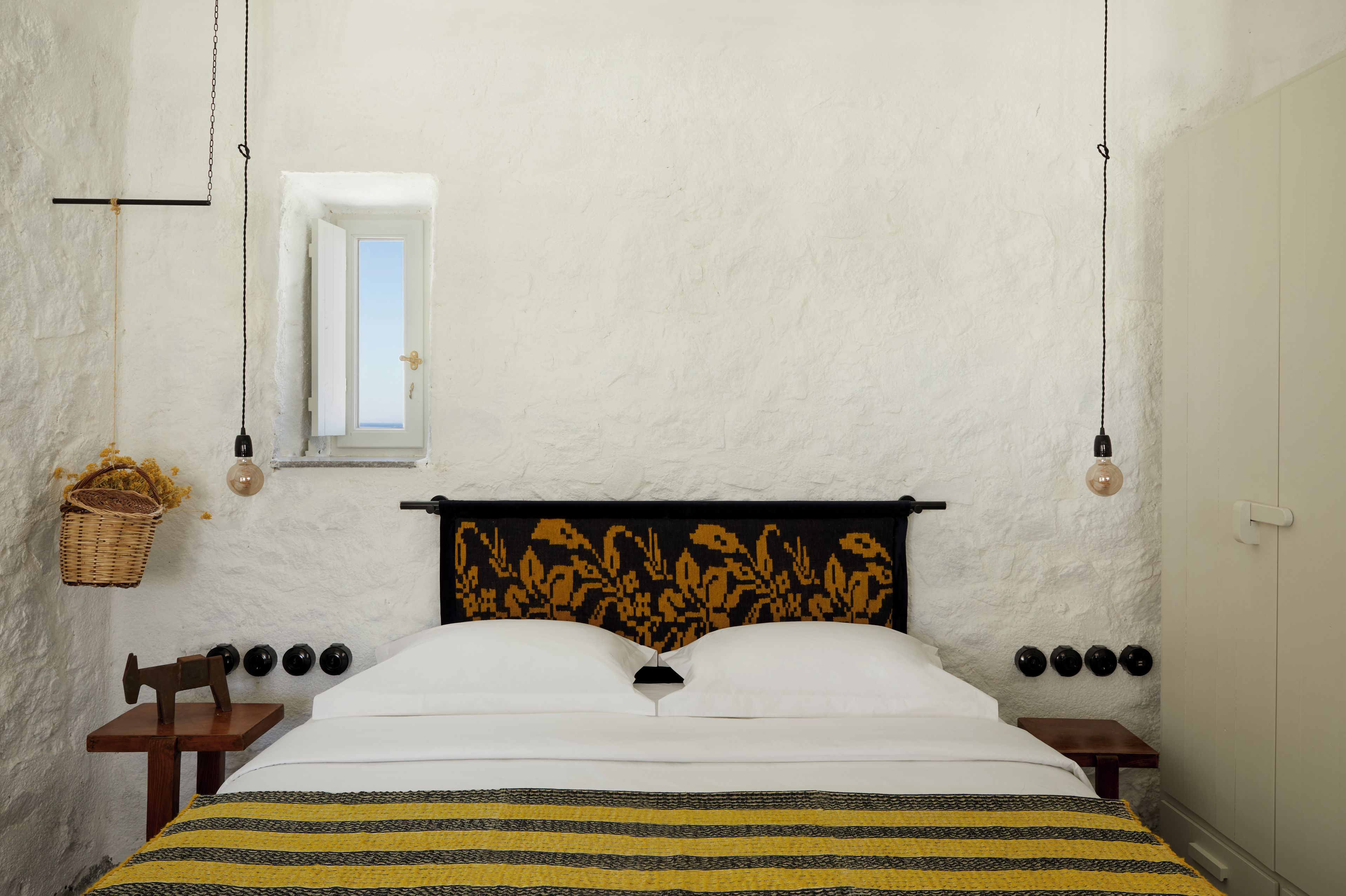 Une chambre à coucher comprenant un lit, une fenêtre, un luminaire suspendu et une prise de courant fixée au mur.