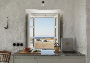 A kitchen with a view of the sea, a wooden cutting board with vegetables, and a sink. - Santa Irini Retreat (Therasia)