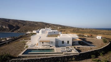 Una villa blanca con piscina, rodeada por un muro de piedra y vistas a un paisaje costero.