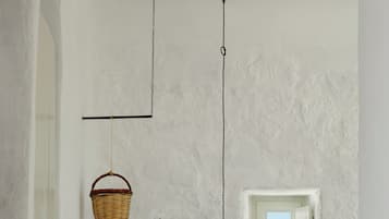 Une chambre à coucher comprenant un lit, une étagère fixée au mur, un panier suspendu, un luminaire et une porte avec une fenêtre.