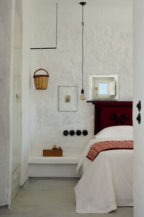 Un dormitorio con cama, estante en la pared, cesta colgante, lámpara y puerta con ventana.