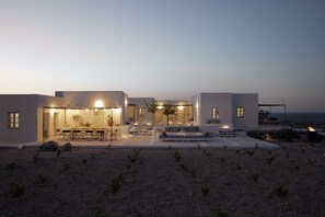 A modern house with a dining area, outdoor seating, and a view of the sea. - Santa Irini Retreat (Therasia)