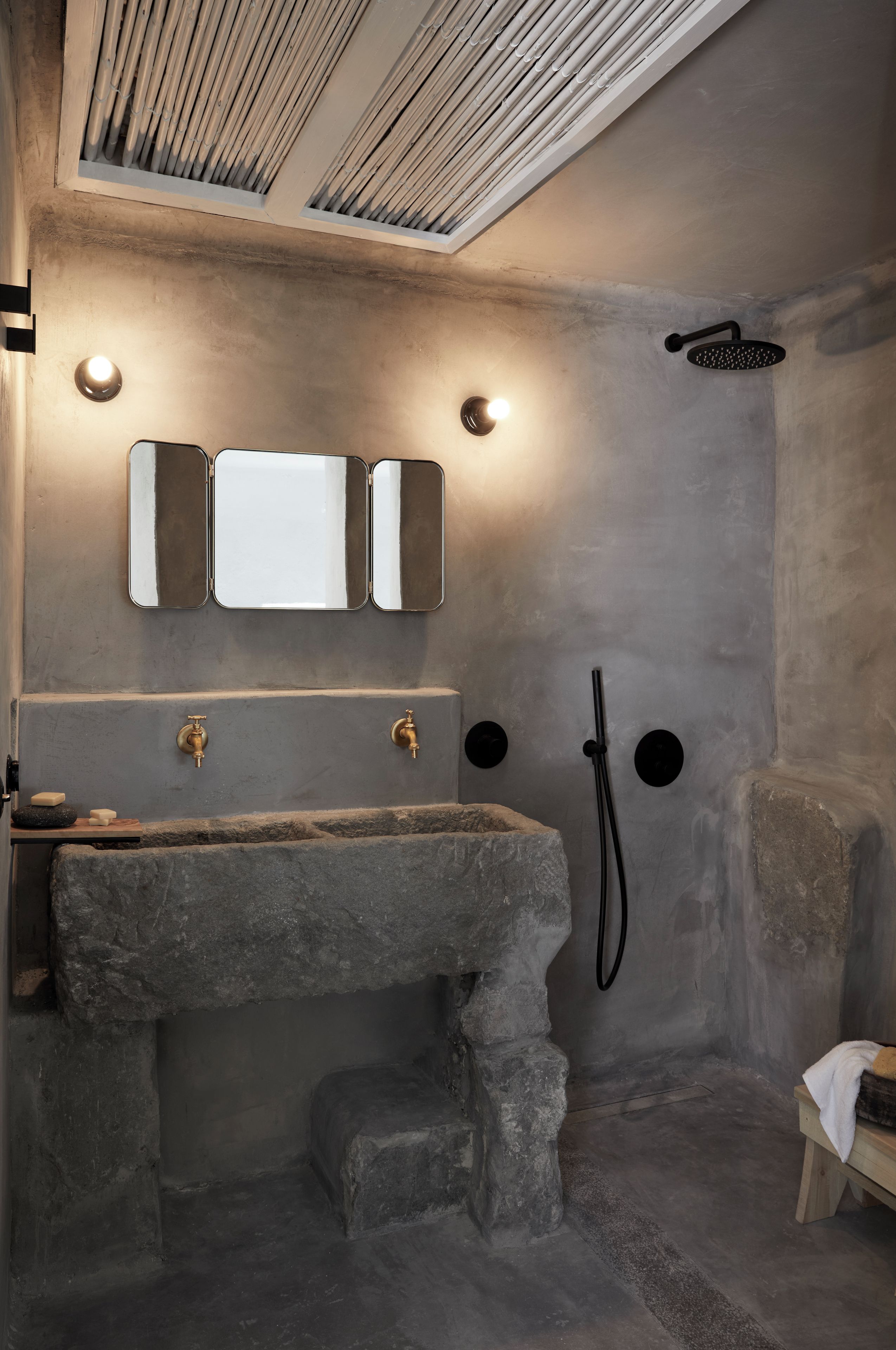 Ein Badezimmer mit einem Steinkonstruktion-Waschbecken, zwei Wandleuchten, einer Dusche und einem Spiegel.
