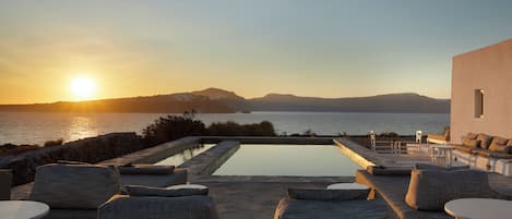 A poolside area with lounge chairs and a view of the sea at sunset.