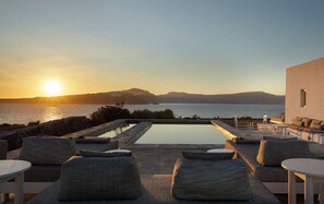 Zona de piscina con sillones de descanso y vista al mar al atardecer.