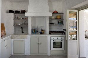 A compact kitchen with white cabinets, a stove, and various kitchen utensils. - Santa Irini Retreat (Therasia)