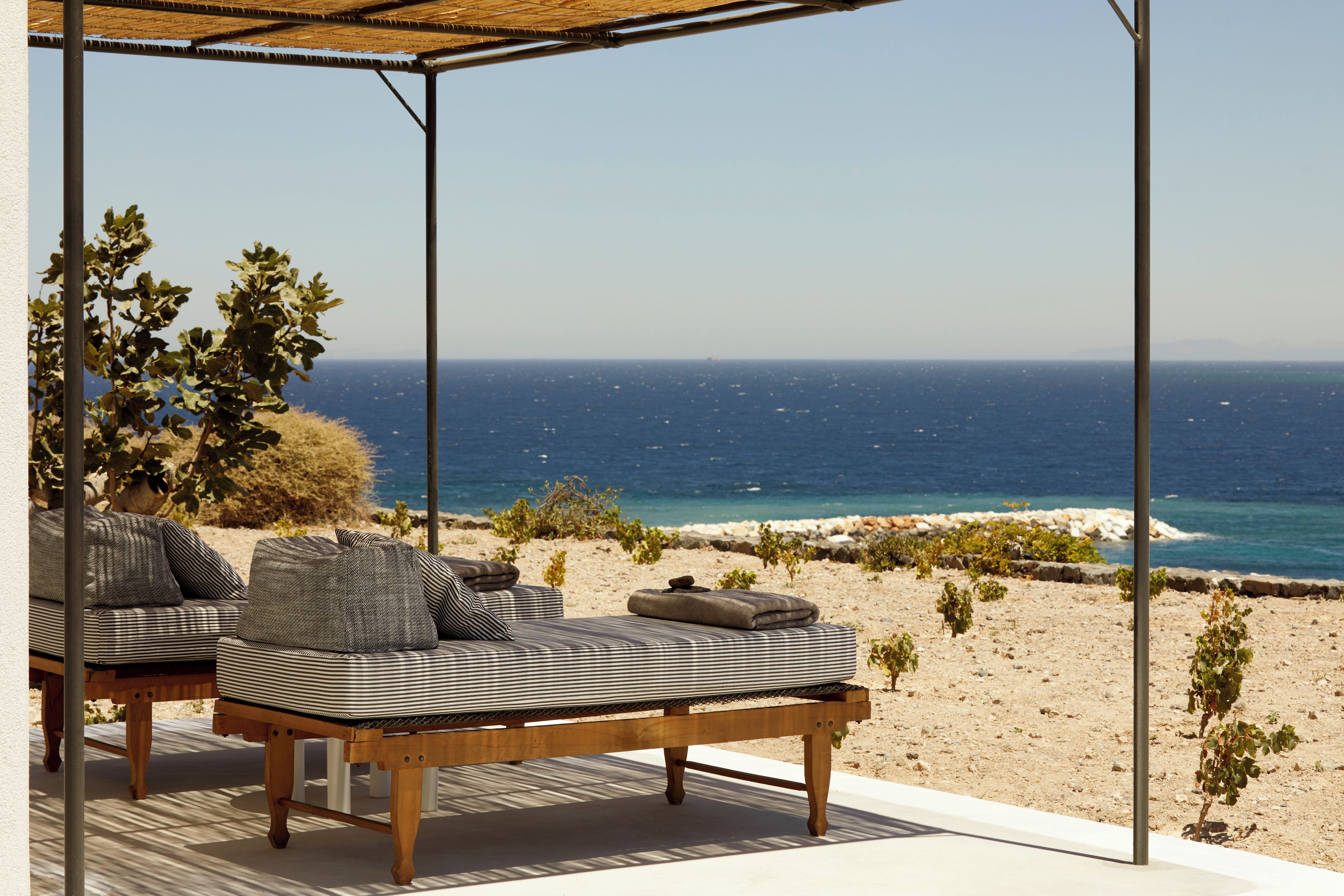 Un salon de plage avec vue sur la mer, comprenant une table en bois et des coussins à rayures.