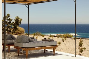 A beachside lounge with a view of the sea, featuring a wooden table and striped cushions. - Santa Irini Retreat (Therasia)