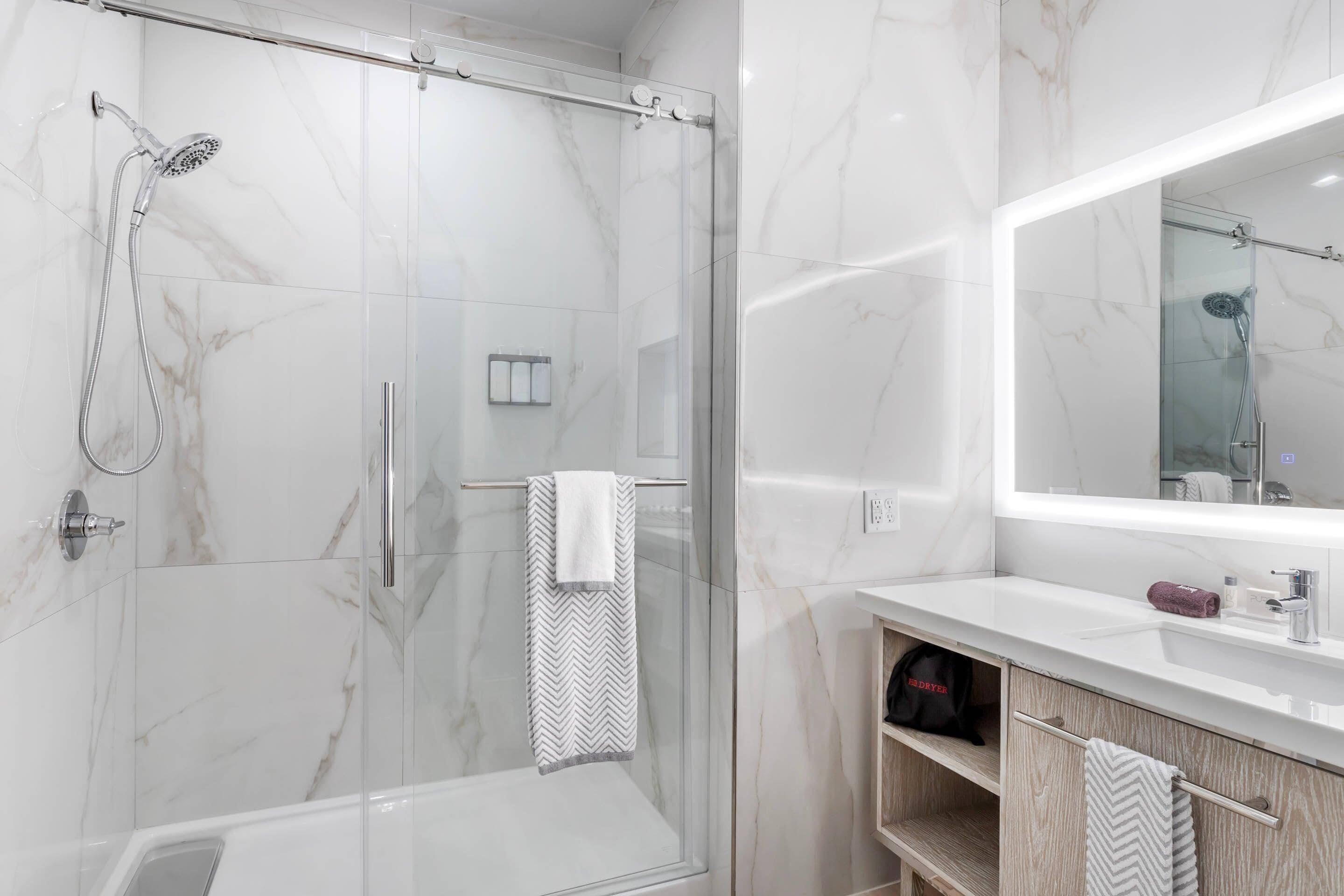 Un baño moderno con ducha envuelta en vidrio, tocador con espejo y perchero.