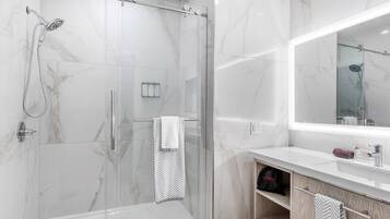 Un baño moderno con ducha envuelta en vidrio, tocador con espejo y perchero.