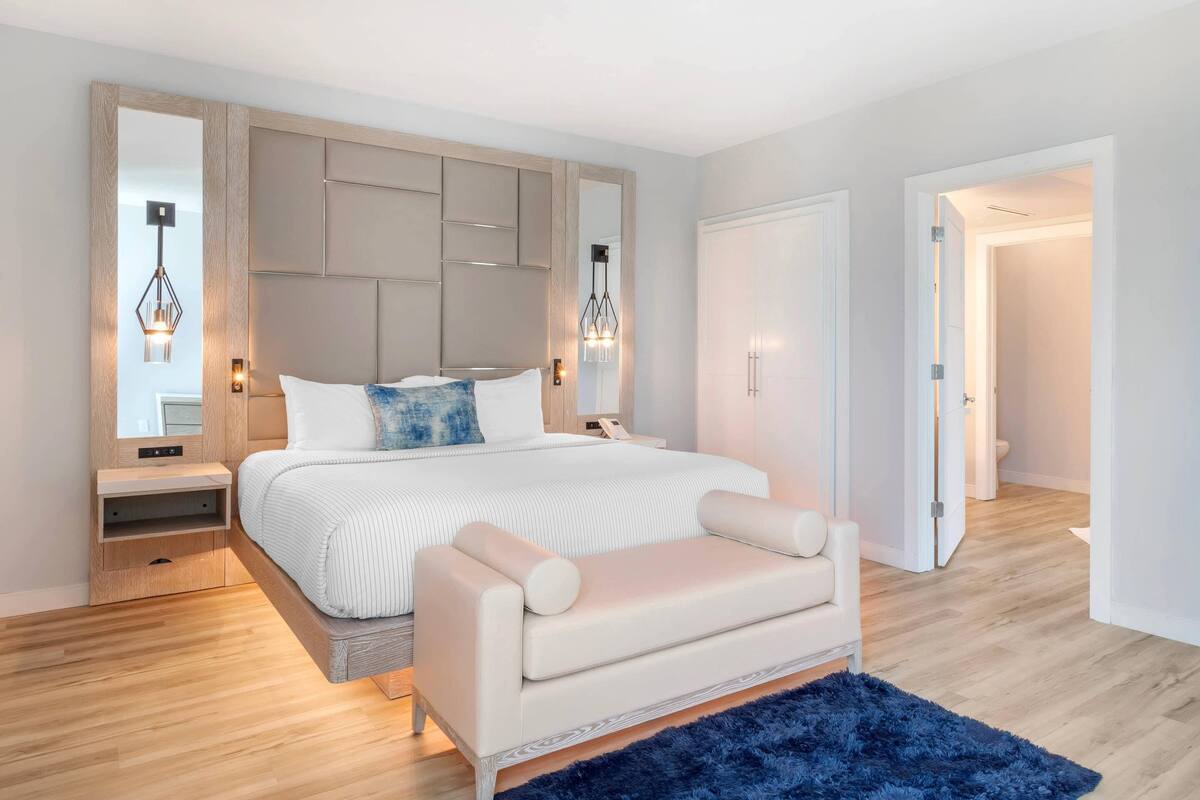 A modern bedroom with a large bed, bedside tables, a nightstand, a sofa, and a blue rug.