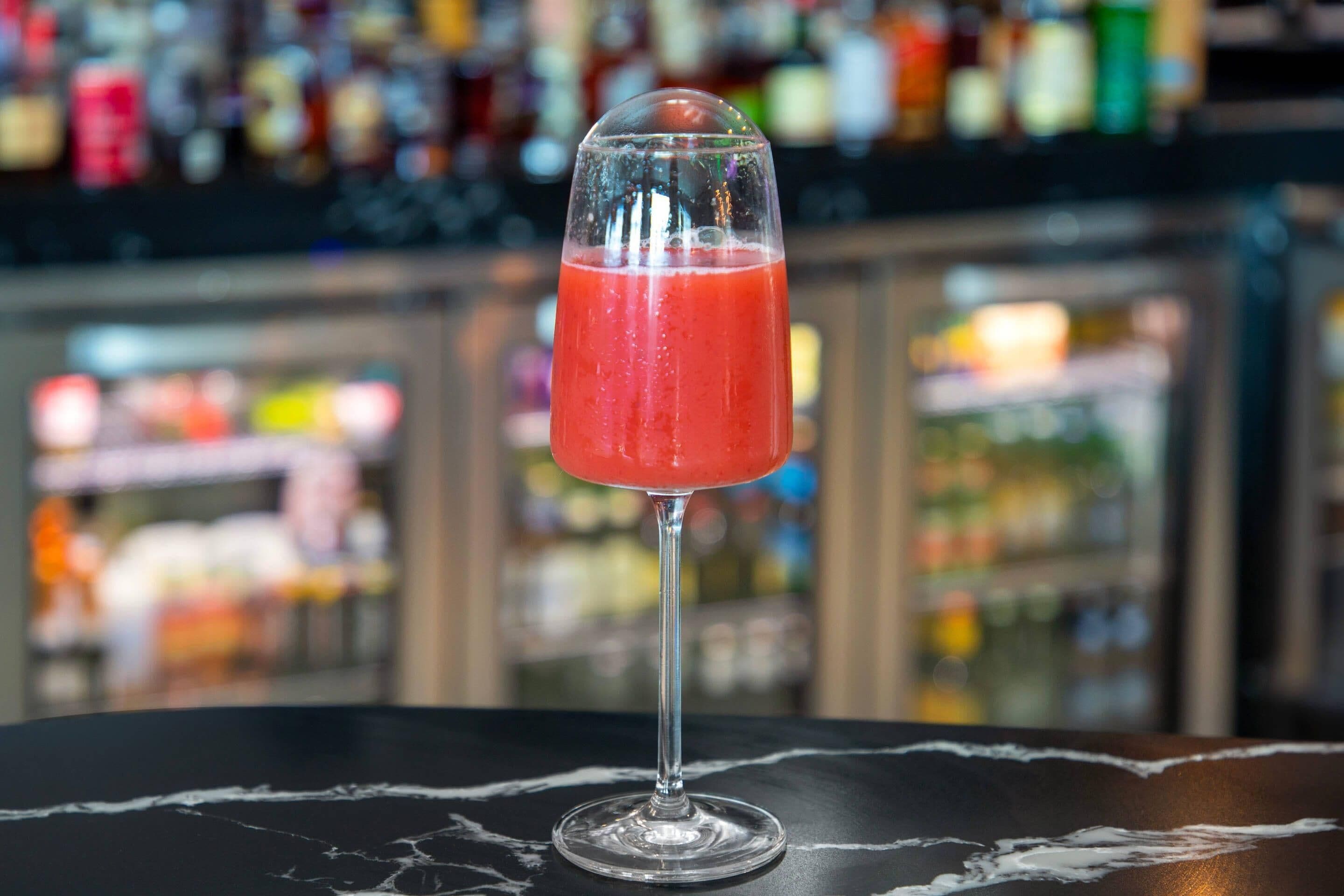 Ein Cocktailglas auf einer Marmorplatte, im Hintergrund verschwommen eine Bar.