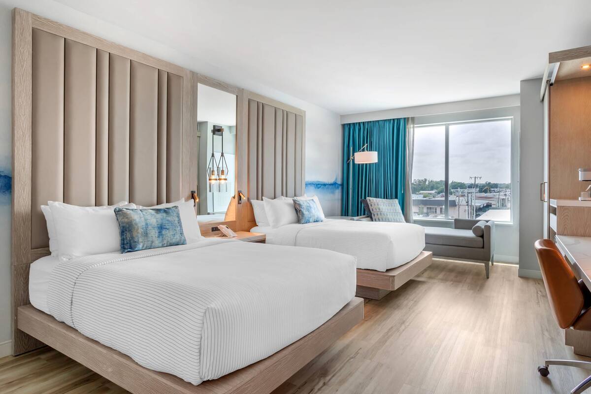 A hotel room with two beds, a desk, and a large window with a view.