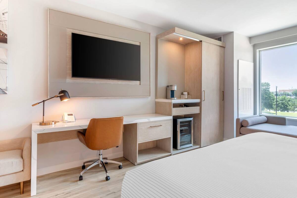 A modern bedroom with a large bed, a desk with a computer, a chair, and a built-in wardrobe.