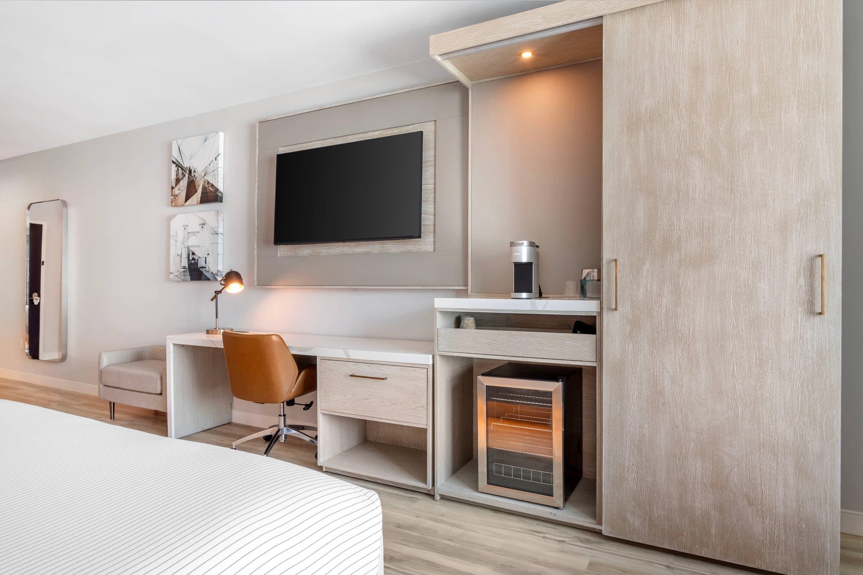 A modern bedroom with a bed, a desk with a chair, a TV, and a wardrobe.