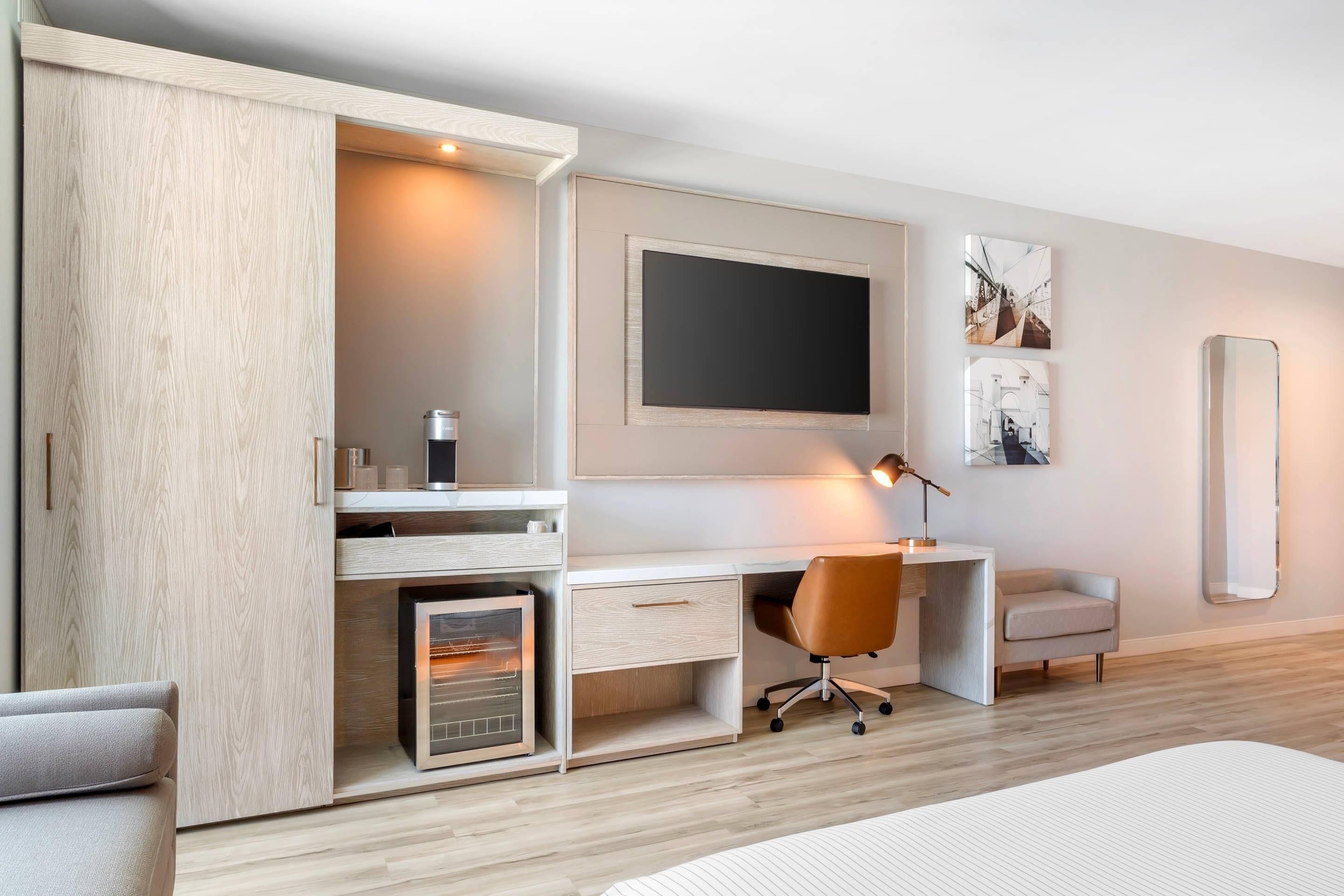 A modern bedroom with a built-in desk, a bed, a wardrobe, and a large mirror.