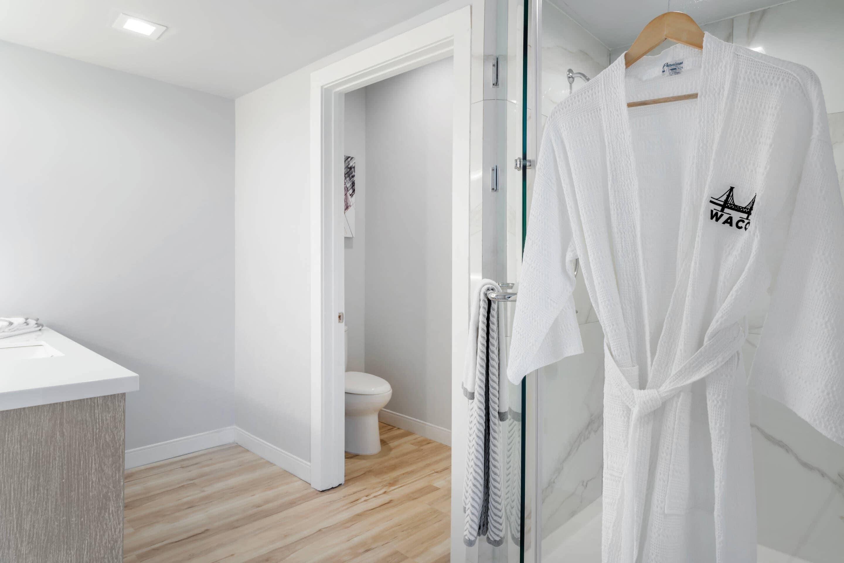 A modern bathroom with a white sink, a glass shower enclosure, and a white robe hanging on a rack.
