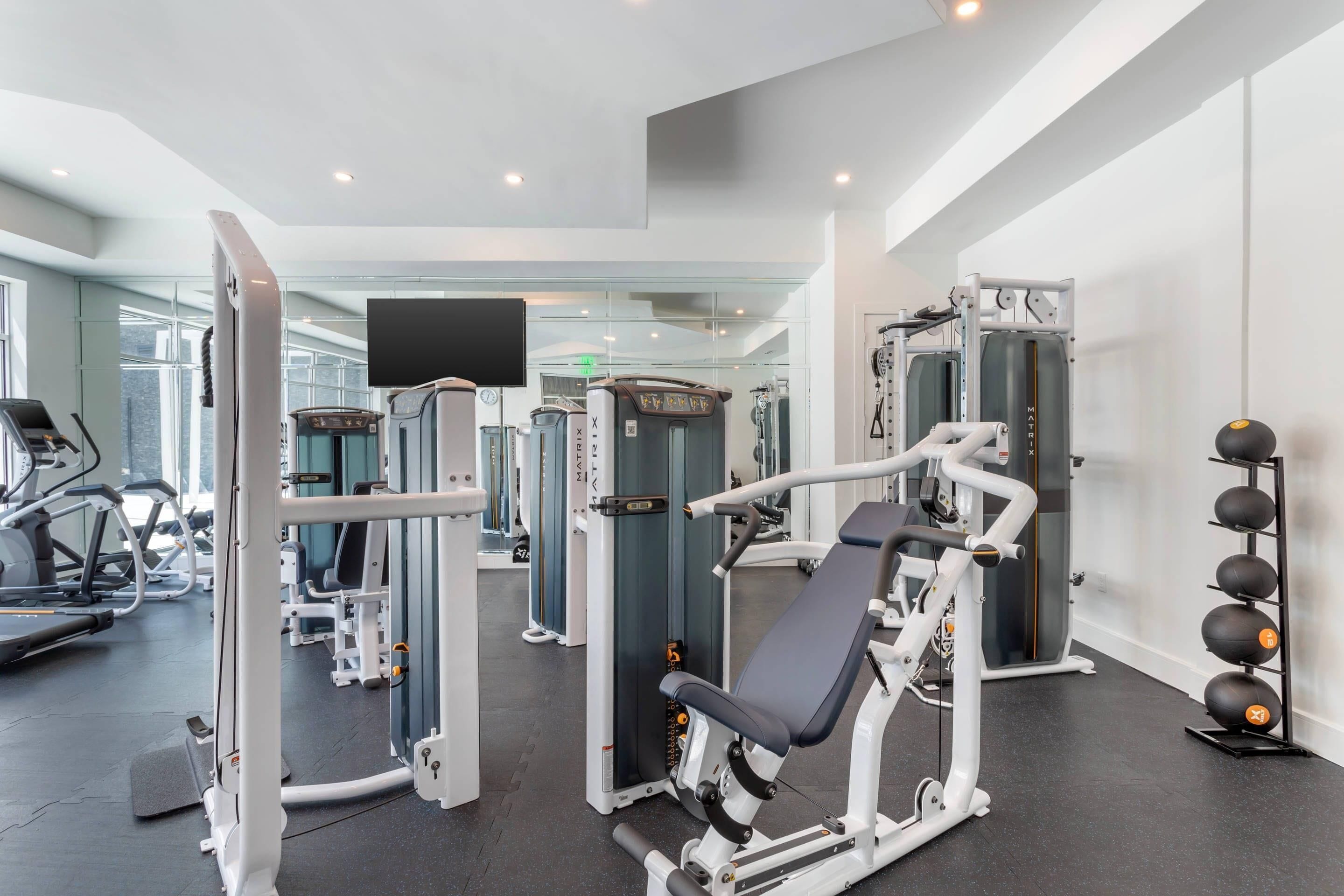 Ein modernes Fitnessstudio mit verschiedenen Trainingsgeräten, einem Fernseher und einem an der Wand befestigten Bildschirm.