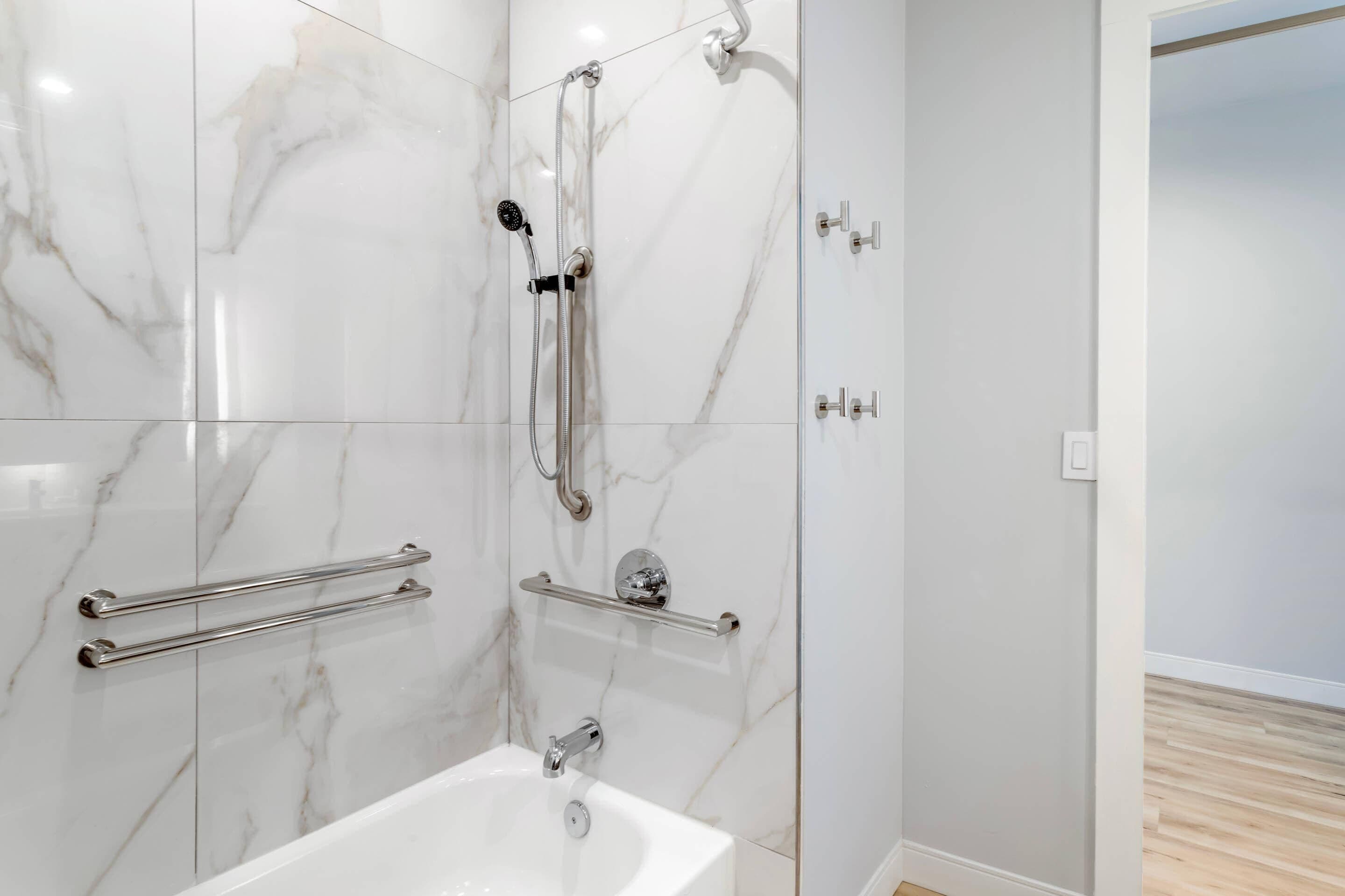 Une salle de bain avec un mur en marbre blanc, une baignoire blanche et une douche équipée d’un pommeau de douche à main.