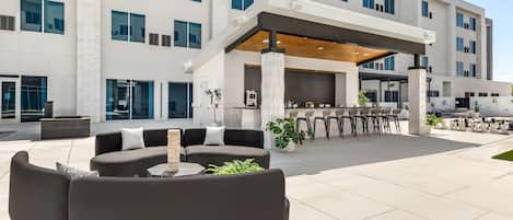A modern hotel exterior with a covered outdoor seating area, large windows, and a clean, contemporary design.
