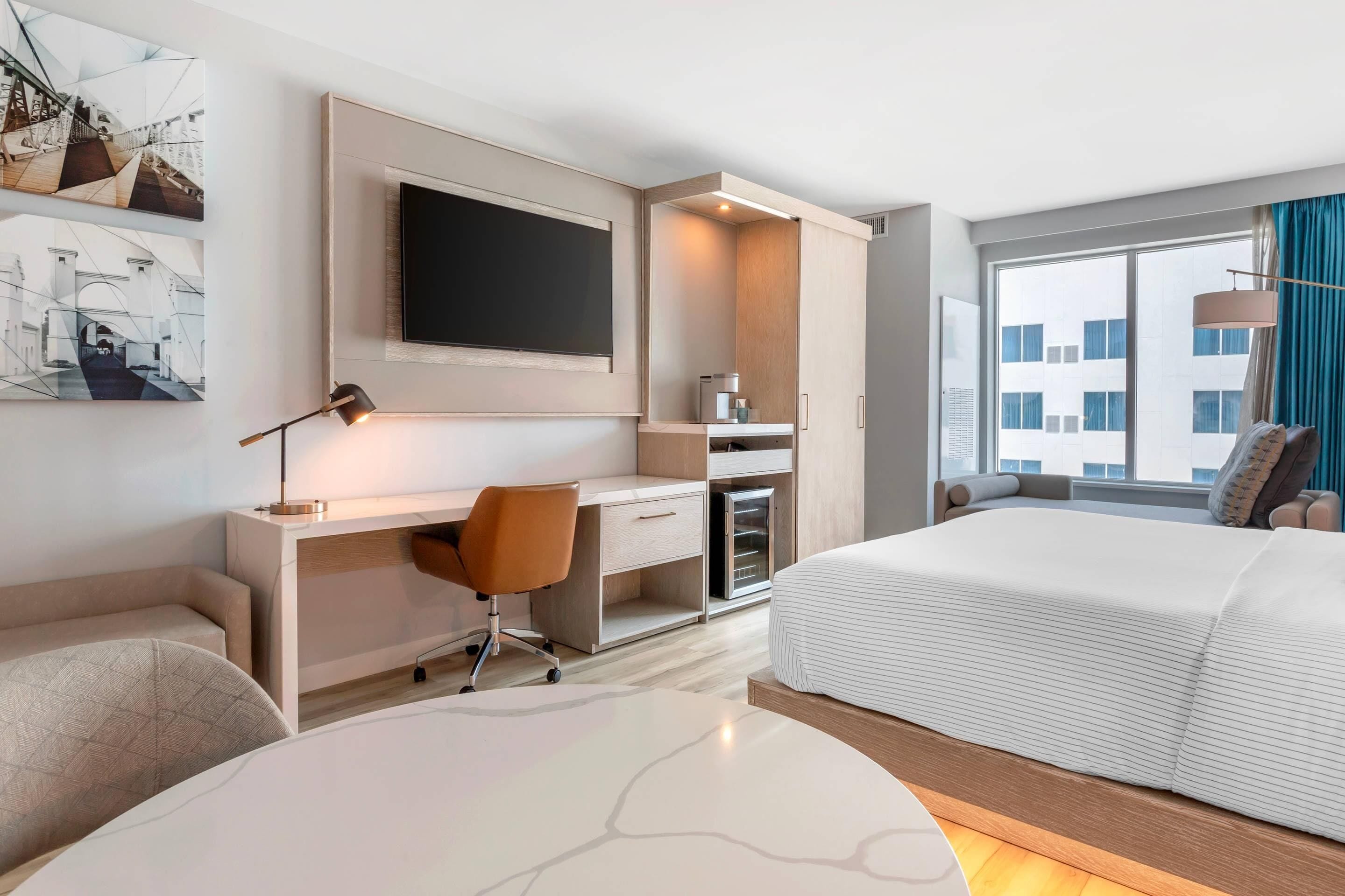 A modern hotel room with a large bed, a desk with a chair, a flat-screen TV, and artwork on the wall.