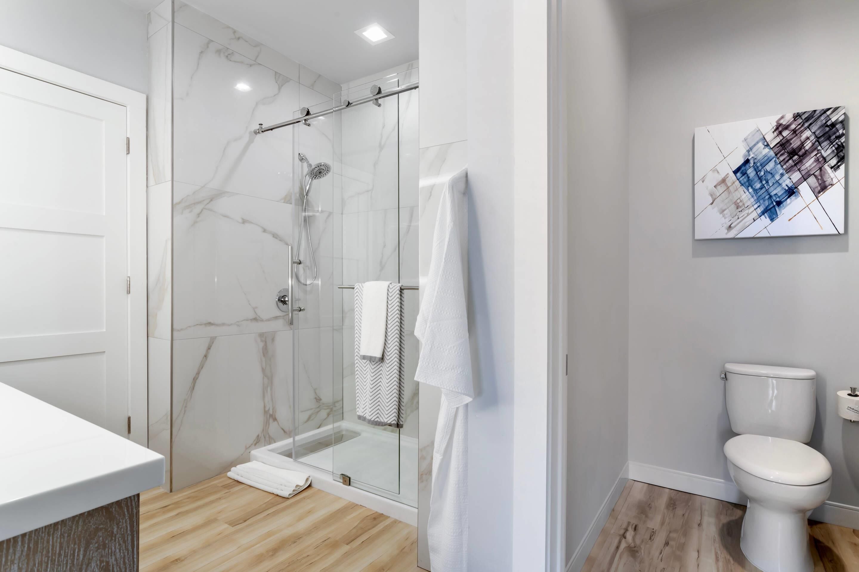 A modern bathroom with a glass-enclosed shower, a white toilet, and a marble wall.