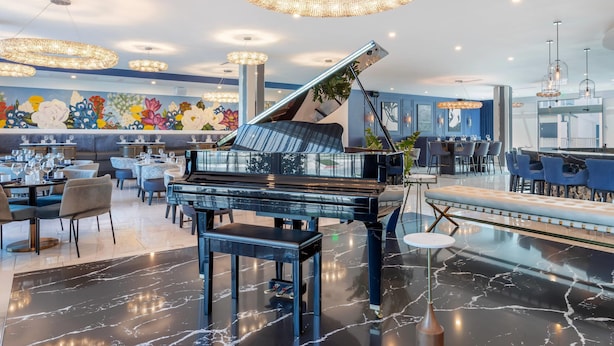 A modern hotel lobby with a grand piano, marble flooring, and elegant chandeliers. - Cambria Hotel Waco Univ Riverfront (Waco)