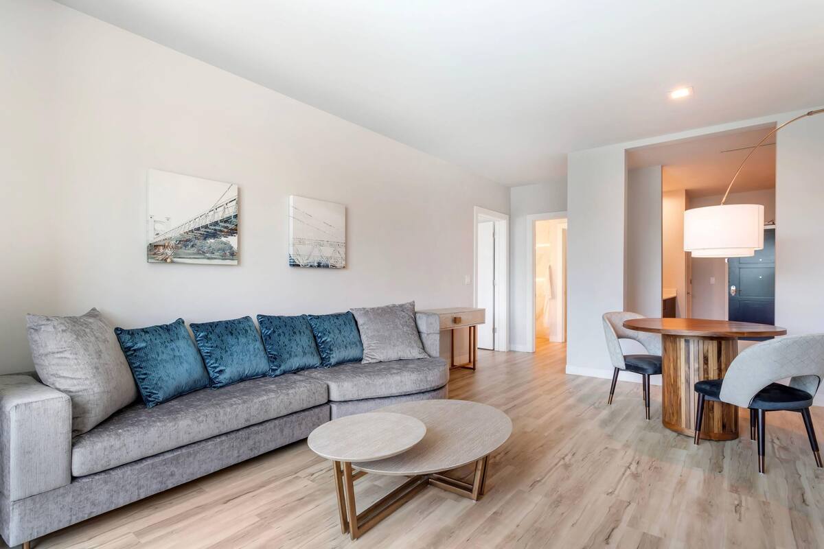 A modern living room with a grey sofa, a round coffee table, and a dining area with a wooden table and chairs.
