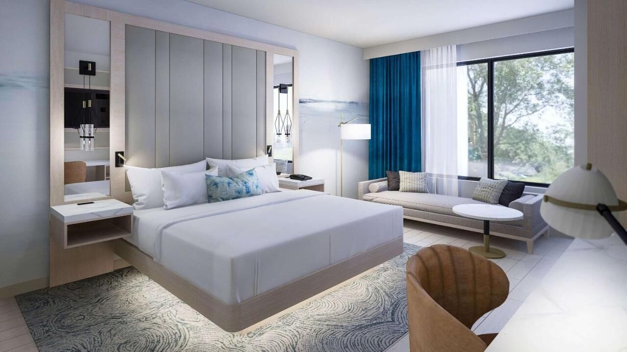 A modern hotel room with a large bed, a sofa, a desk, and a window with a view.