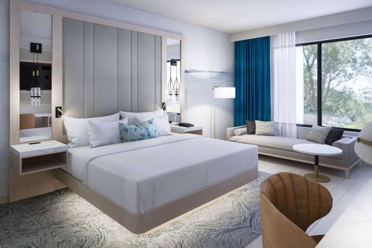 A modern hotel room with a large bed, a sofa, a desk, and a window with a view.