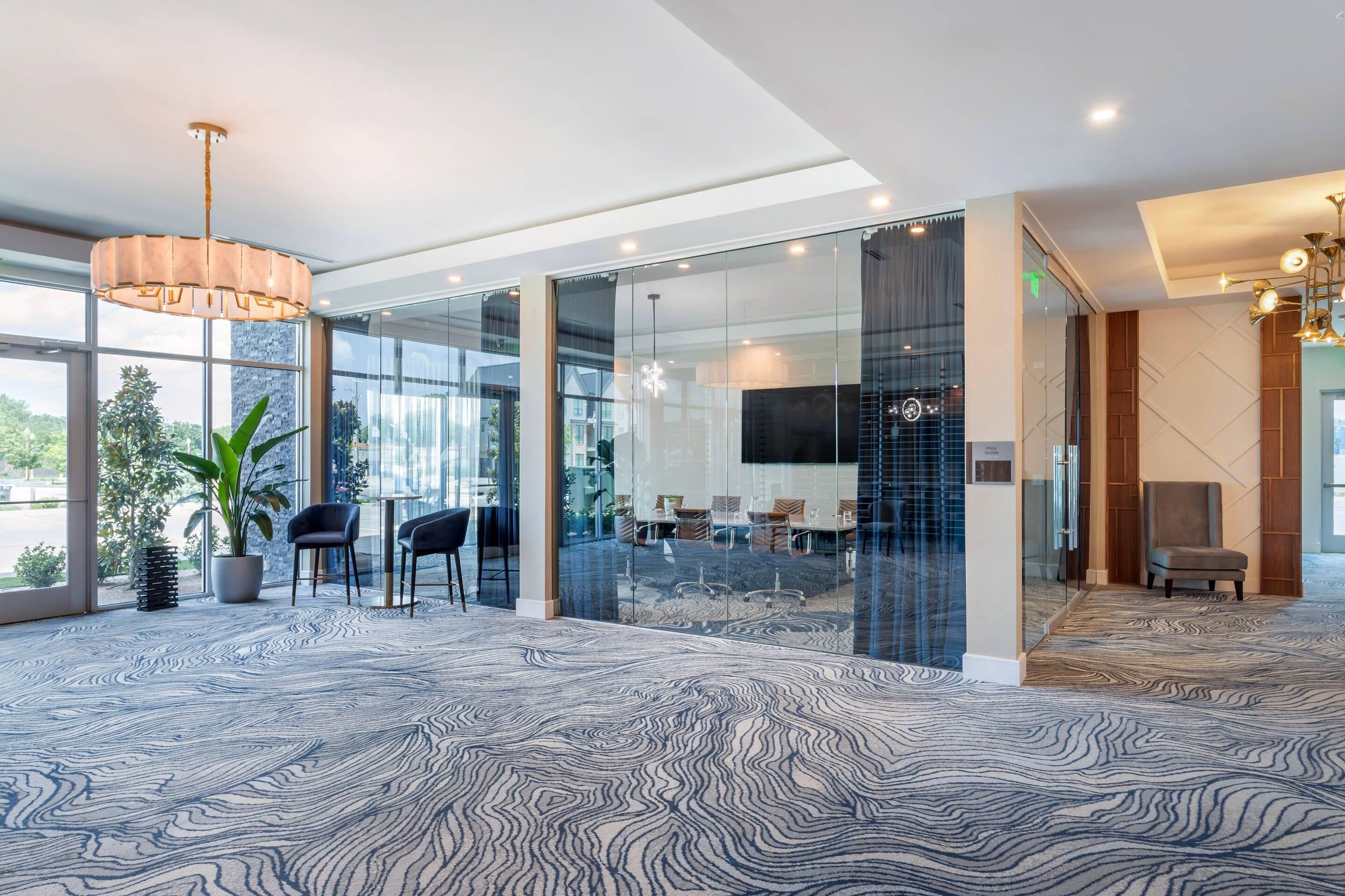Un hall d’entrée moderne avec un tapis à motifs, des murs en verre, un espace salon et un grand lustre.