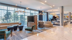A spacious living area with a large TV, comfortable seating, and a piano. - Cambria Hotel Waco Univ Riverfront (Waco)