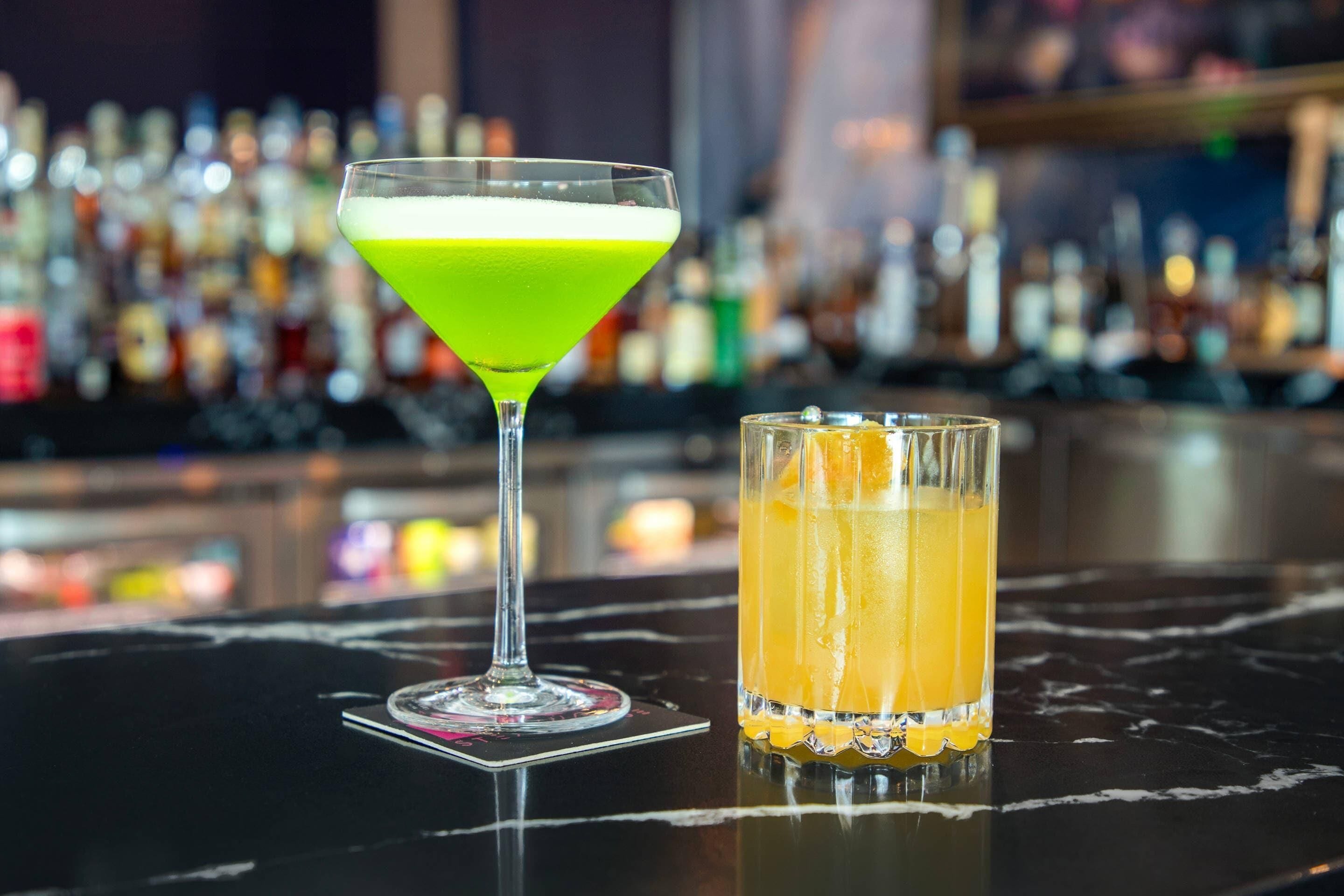 A bar with a martini glass and a highball glass on a marble surface.