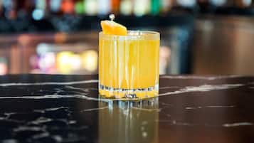 A clear glass of orange juice with a garnish on a reflective surface, likely a bar counter.