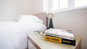 A neatly made bed with white linens, a bedside table with a lamp, and two books titled 'Getting Things Done' and 'Tribe of Mentors'. - Sandall Apartment (Doncaster)