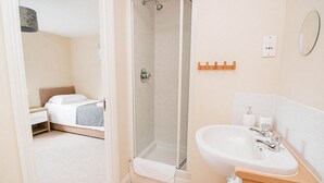 A bathroom with a shower, a sink, and a bed in the adjacent room. - Sandall Apartment (Doncaster)